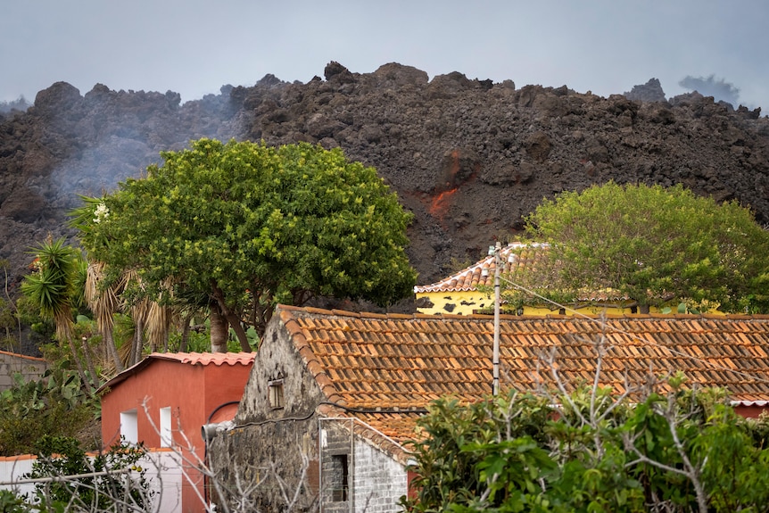 Los techos de las casas están en primer plano, las copas de los árboles detrás.  Detrás de eso, una roca gigante negra y naranja se alzaba