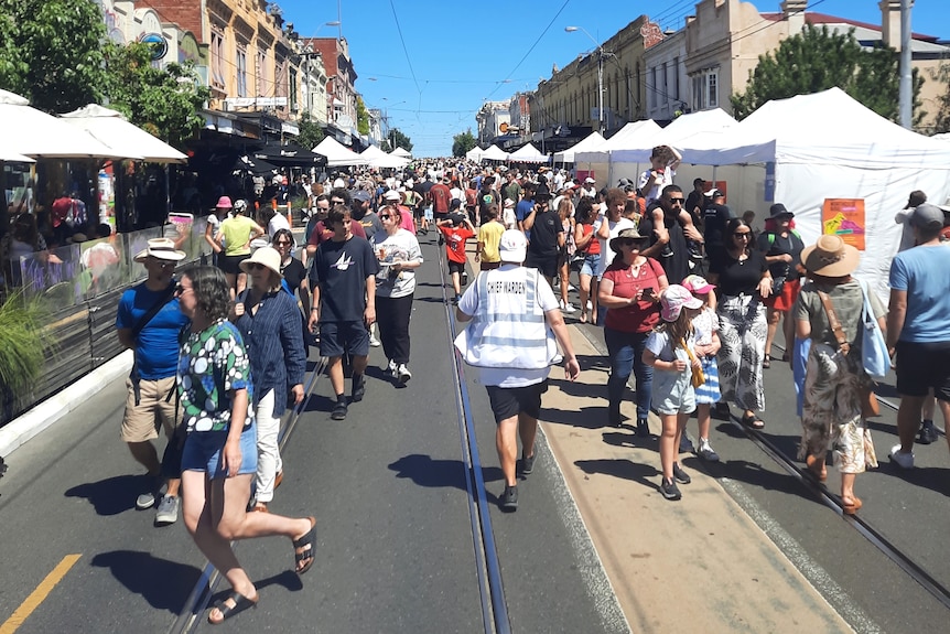 A crowd of people walk along a street closed off for a community festival. 