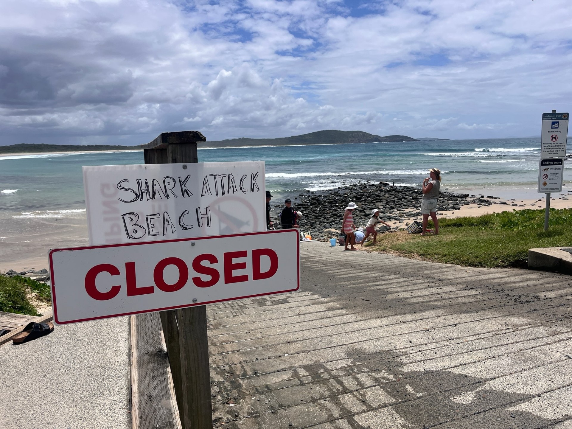 A makeshift shark attack beach closed sign at a boat ramp with ocean in background.