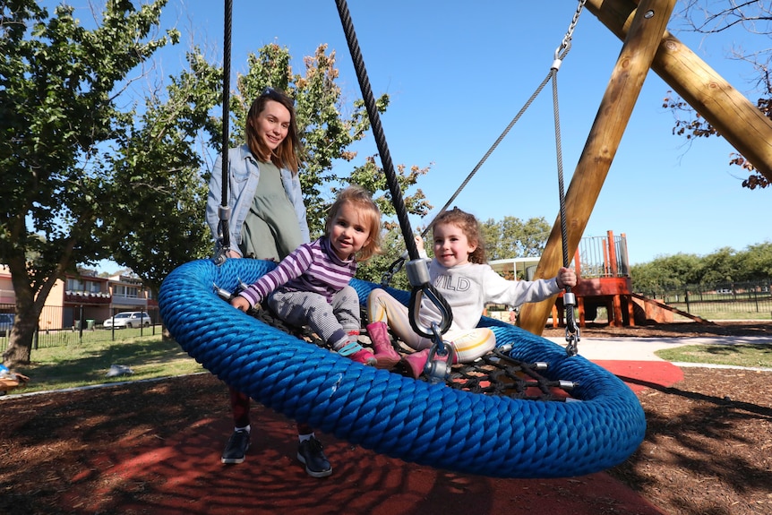 Two kids on a swing are pushed by their mother