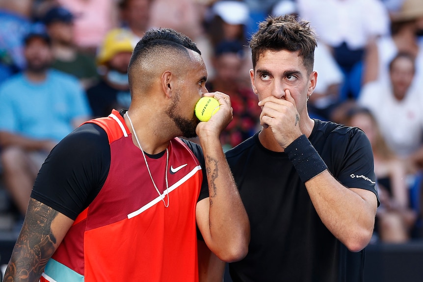 Two Australian male tennis players chat during a doubles match.