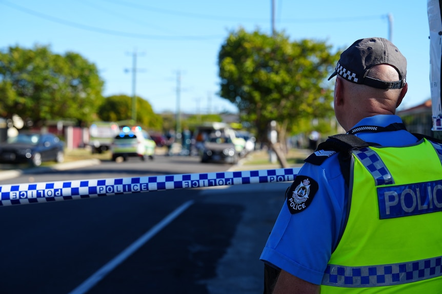 A police officer wearing a high-vis vest standing in front of police tape around a crime scene