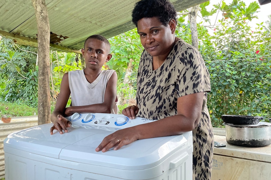 A woman and boy leaning on a washing machine 