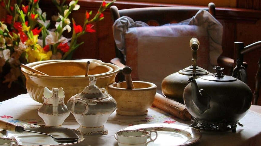A tea setting with an empty chair, tea cups, saucers, and mixing bowls with a bunch of gladioli in the background
