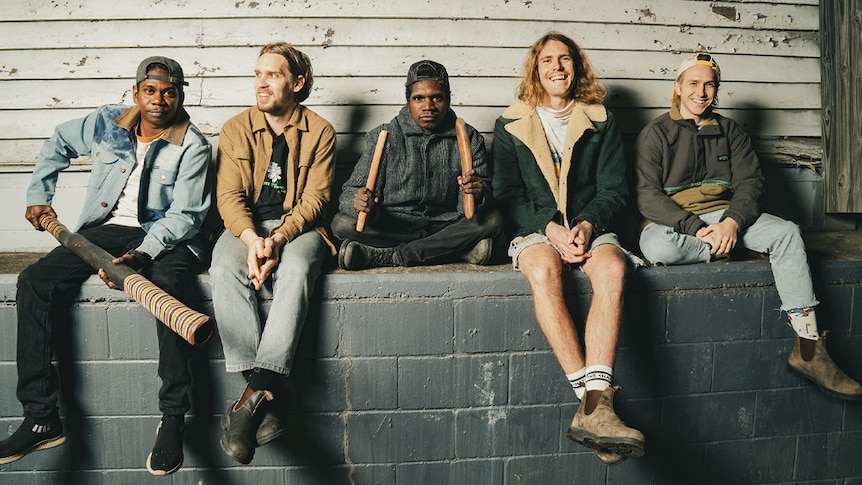 The five members of King Stingray sit in front of a timber background on a brick platform, facing the camera.