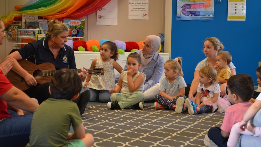 Woman plays guitar at childrens playgroup while children watch carefully