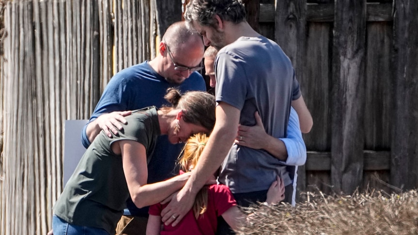 Adults huddle together with a a child as they pray outside the Woodmont Baptist church.