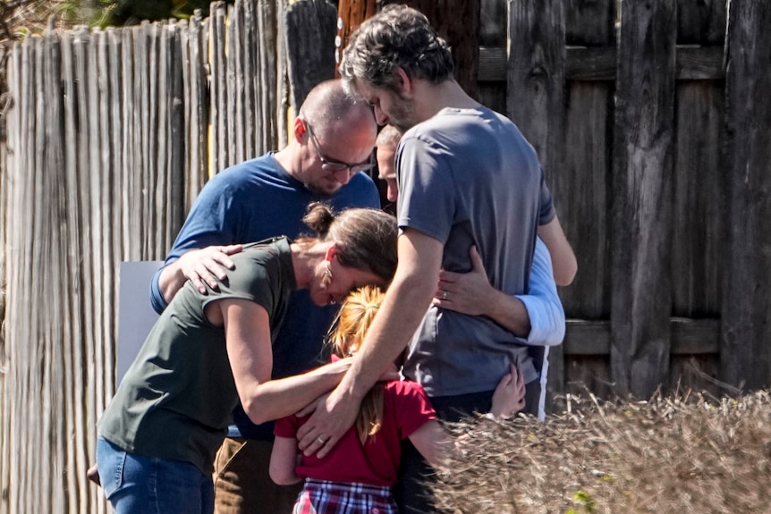 A family hugs each other closely as they pray.