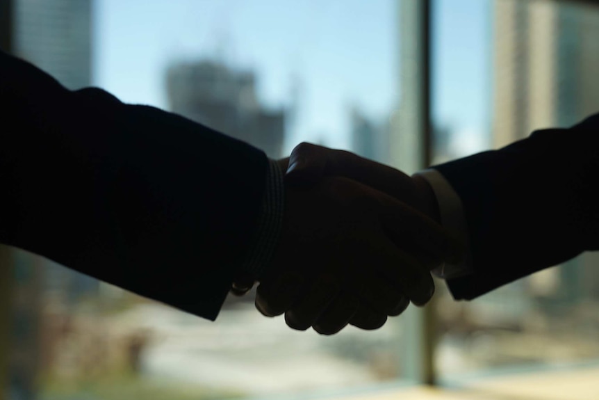 Close up dark silhouette of two people shaking hands in a corporate office.