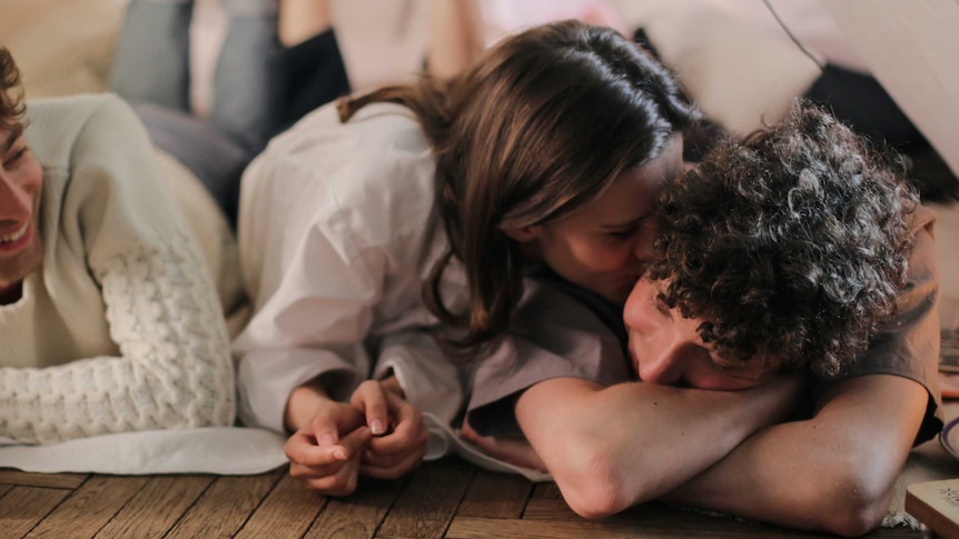 Three people laying on the ground smiling in a story about why more women are suggesting open relationships.