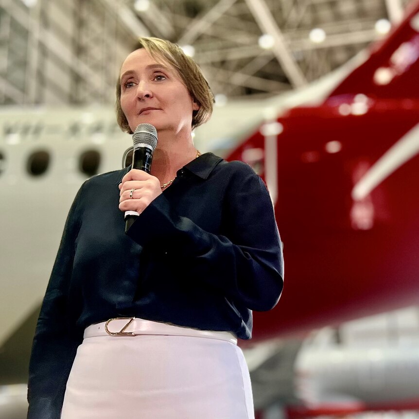 Midshot of Qantas CEO Vanessa Hudson standing in front of Qantas and Jetstar planes in a hanger.