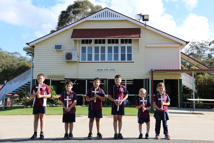 Six students from Maroon State School hold white crosses in front of school building to honour those from the town lost in WWI.