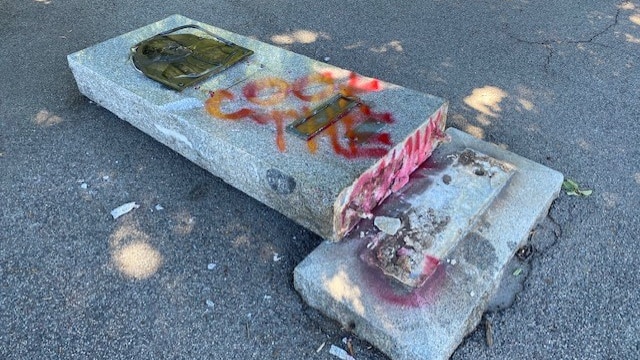 A stone monument toppled over with the words "cook the colony" graffitied on the stone in red paint