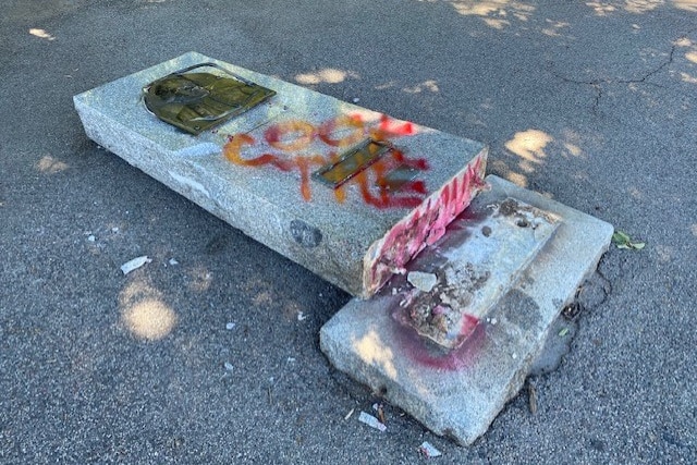 A stone monument toppled over with the words "cook the colony" graffitied on the stone in red paint