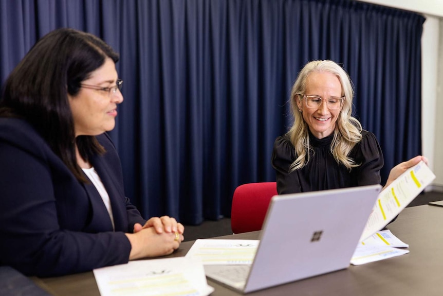 (LtoR) Grace Grace and Stacie Hansel sits at a table in an office with a laptop.