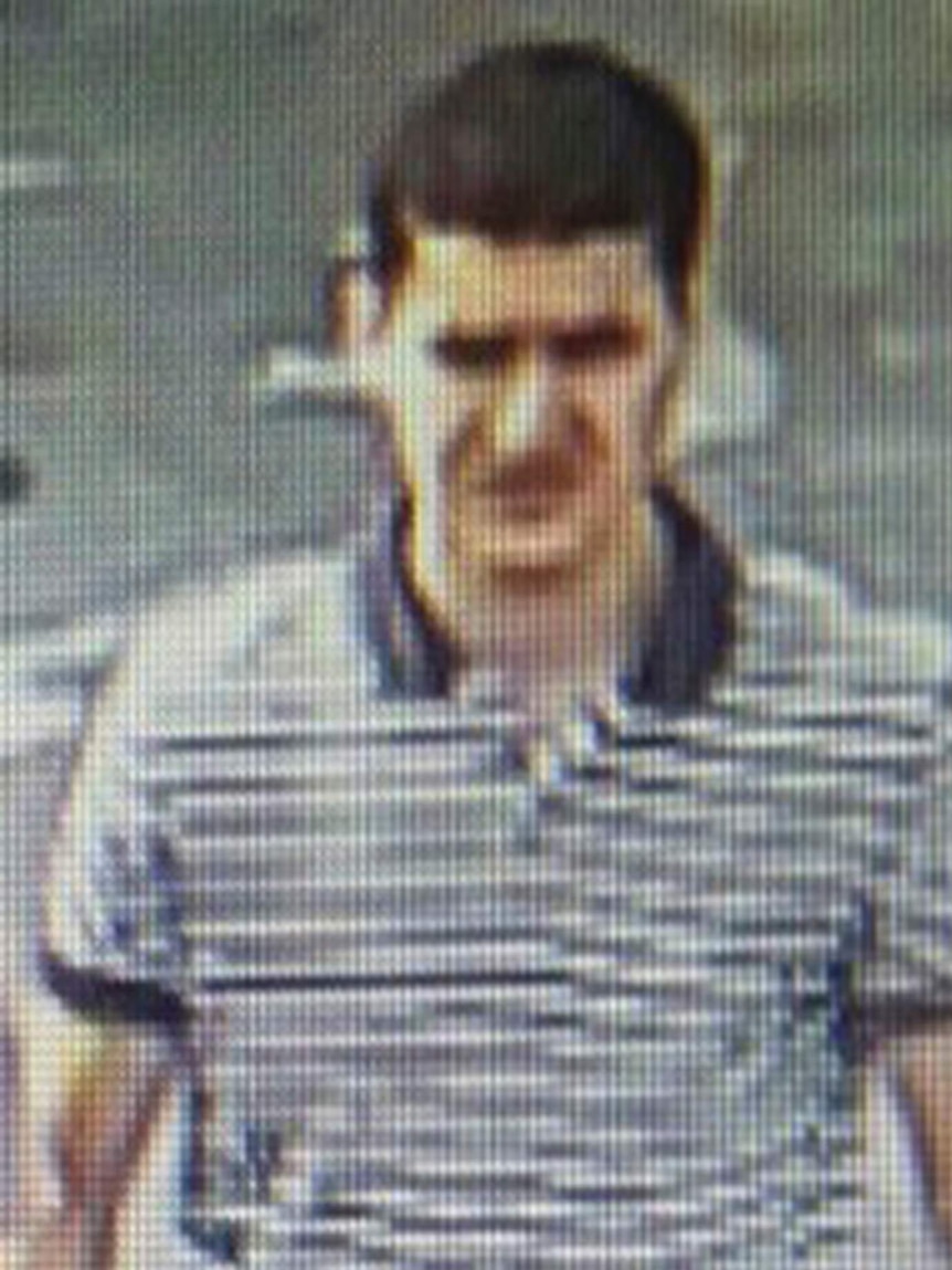 A grainy image of a dark-haired man in a striped polo shirt.
