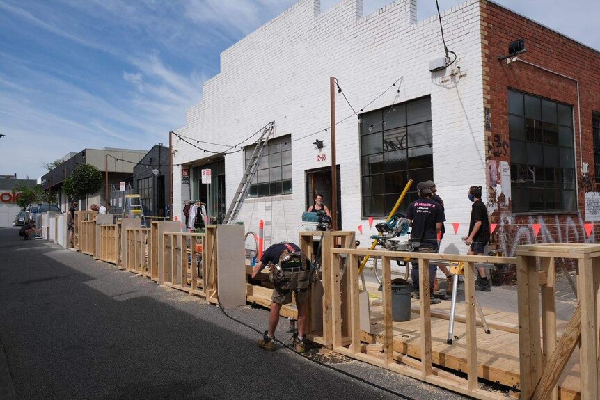 Workers build a wooden platform over a street.