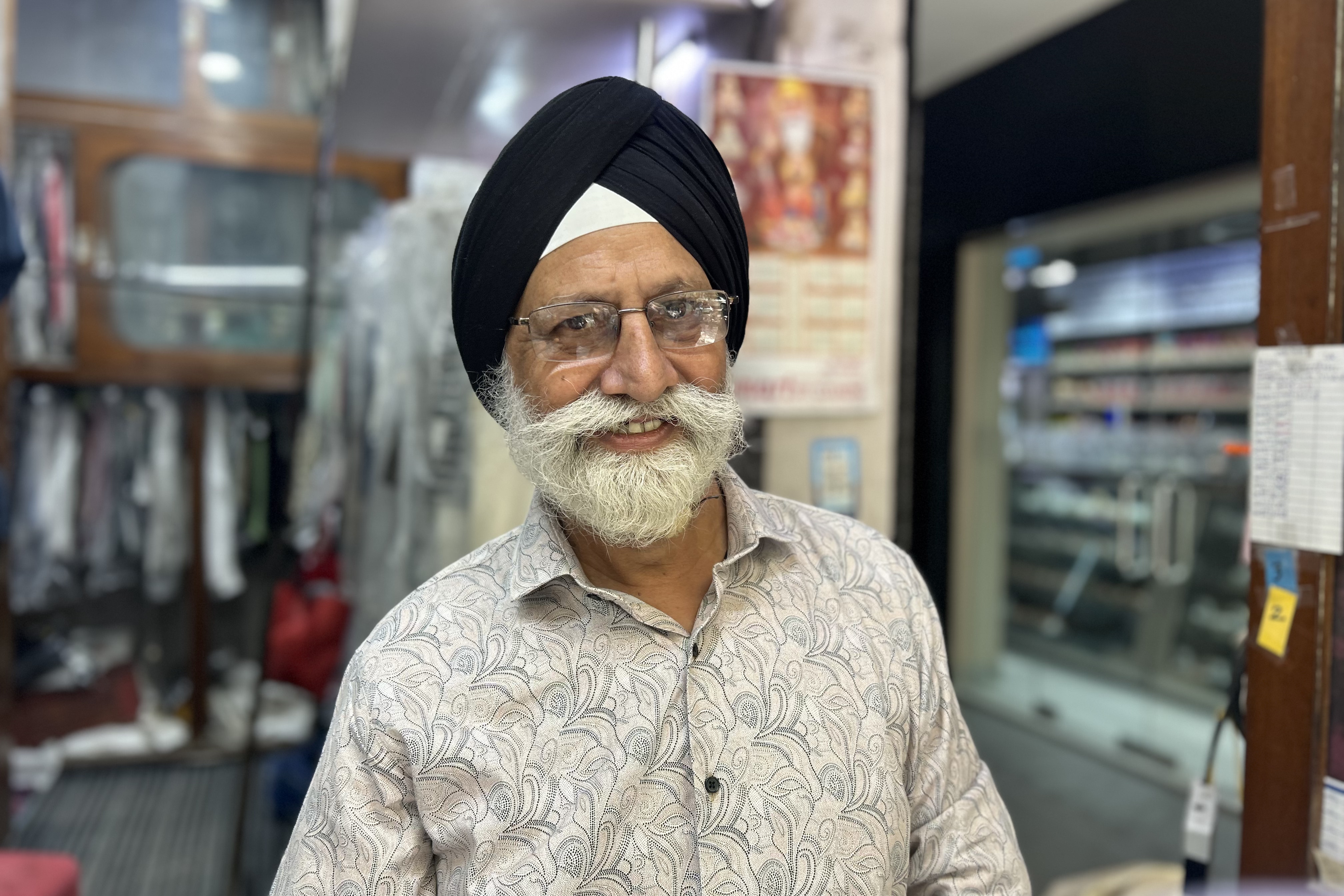 A sikh man, with black turban and grey beard smiles at the camera.
