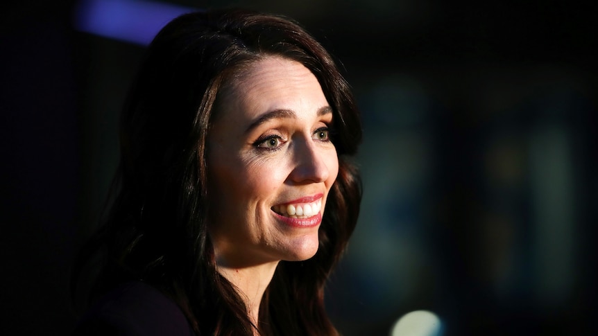 A close up of Jacinda Ardern smiling while talking in front of a microphone.