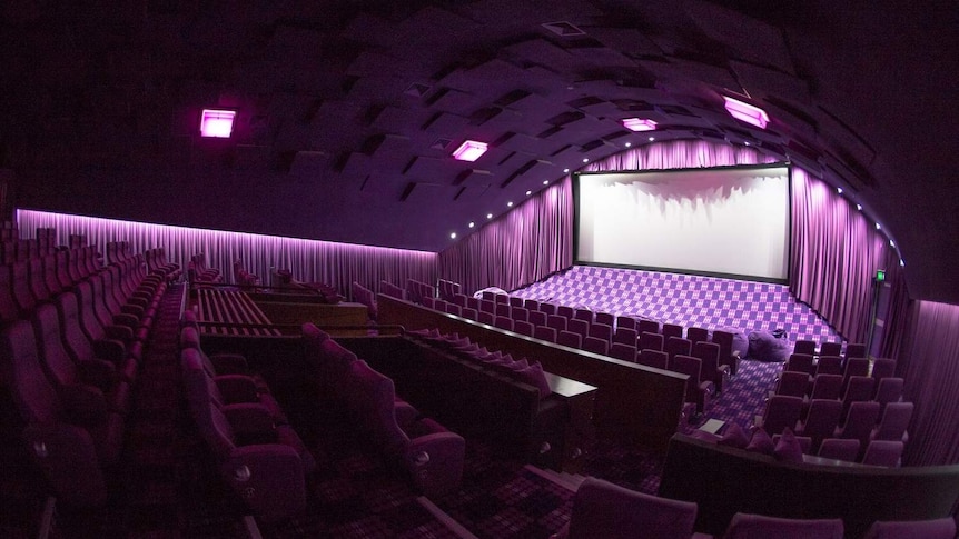 A movie screen and seating in a purple-lit empty cinema at the New Farm Cinemas in inner-city Brisbane.