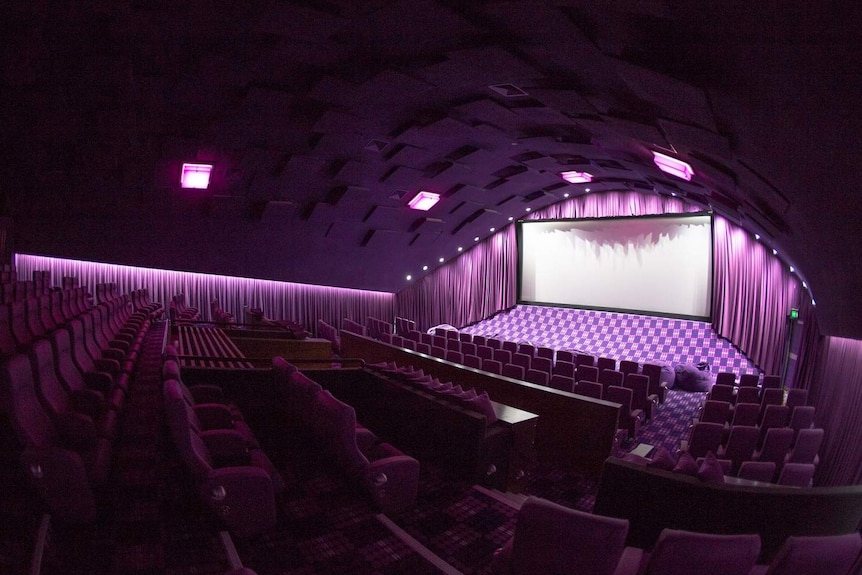A movie screen and seating in a purple-lit empty cinema at the New Farm Cinemas in inner-city Brisbane.