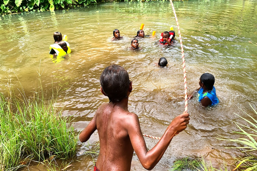 A child throws a rope to kids in a river at Warmun.