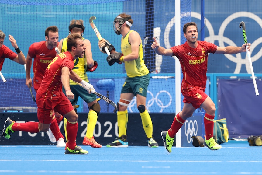 A man in a red shirt raises his arms out wide while holding a hockey stick