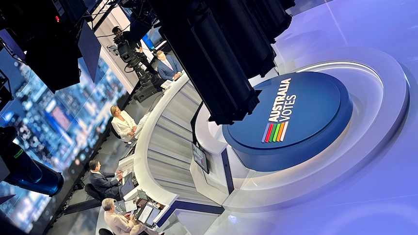 Aerial shot of four people sitting at a desk in a TV studio with Australia Votes signage in front.