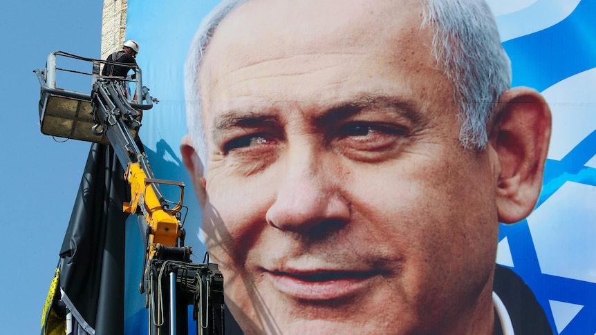 A huge poster of Benjamin Netanyahu being strung up on a building by a man in a cherry picker