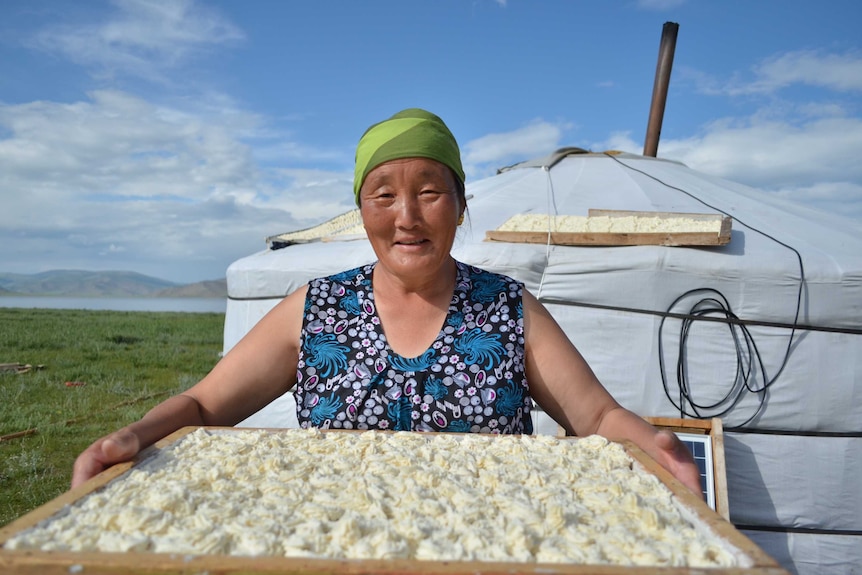 A Mongolian woman smiles holding a crate of food.