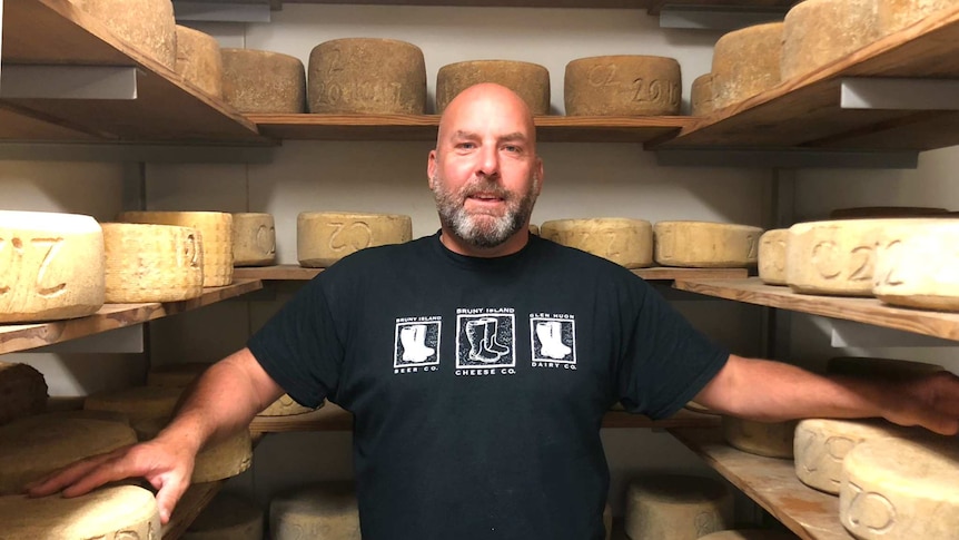 A person standing in their cellar (larder) with multiple cheese wheels all around