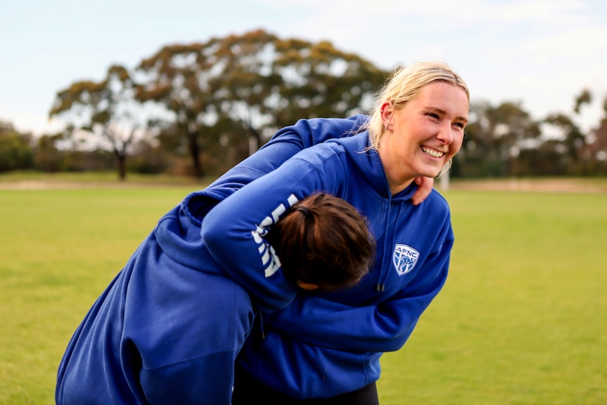 Two young women smile wrestling wearing blue hoodies on a football oval