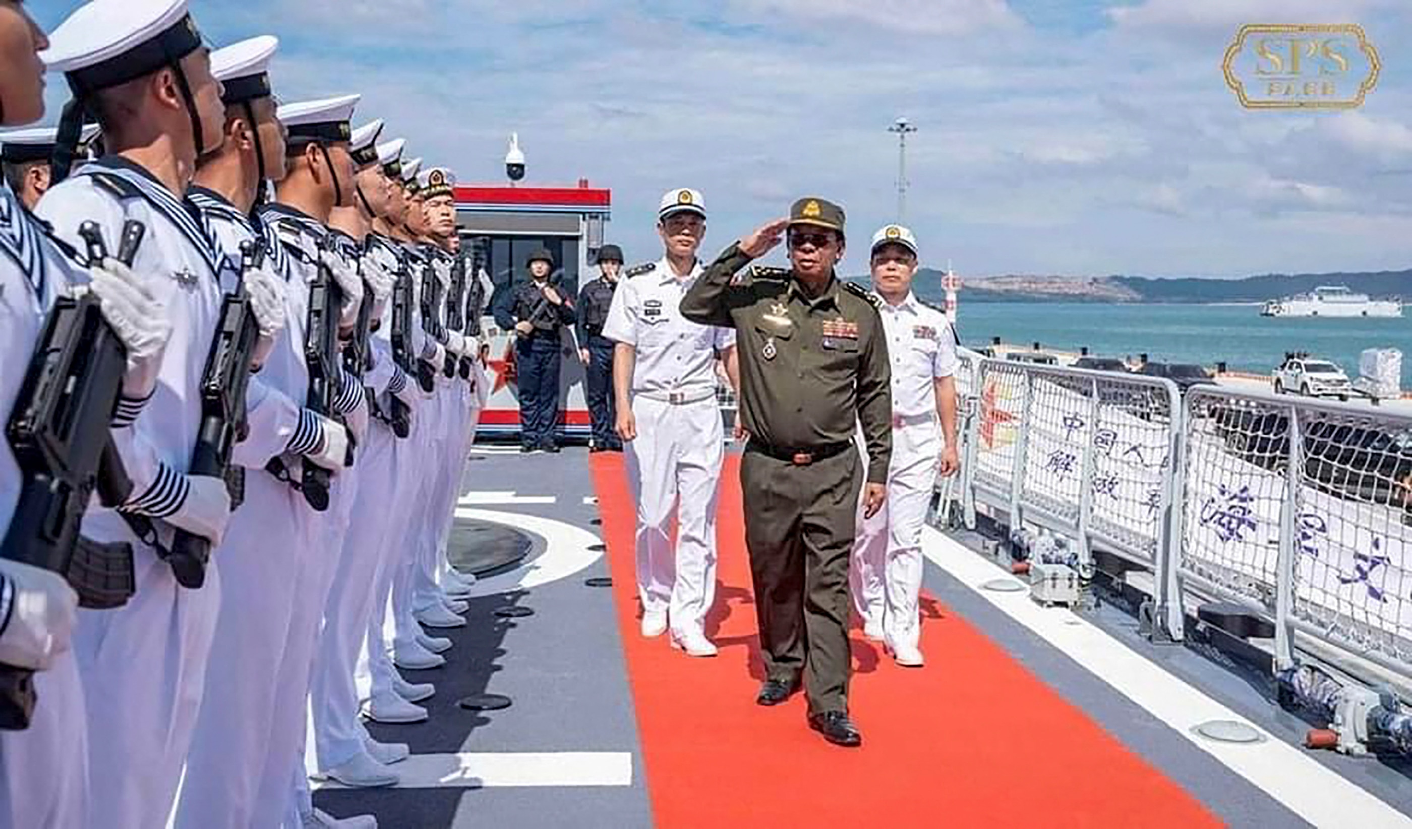 A man in military uniform salutes naval personnel in line holding firearms.