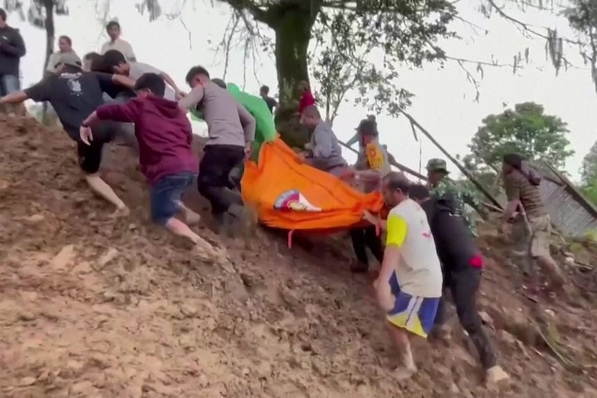 People walk up a muddy slope carrying a sheet containing something heavy.
