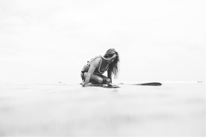 Black and white shot of a female surfer kneeling on her board while on the water
