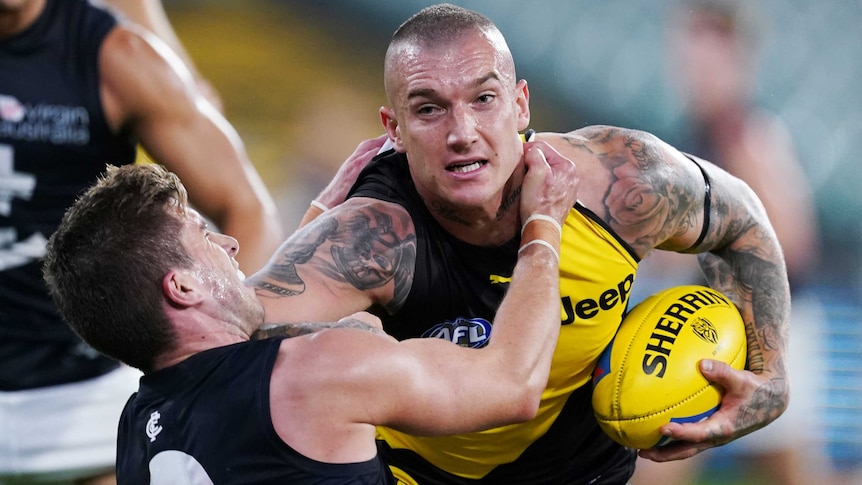 AFL player grips ball in one hand while sticking his arm out to keep away from an opposition tackle.