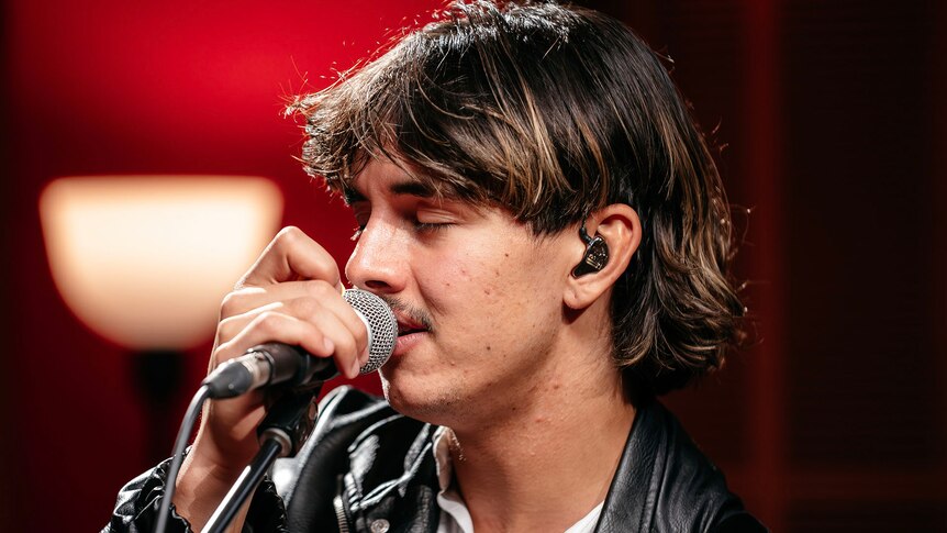 Close up of person singing into a microphone with their eyes closed in a studio