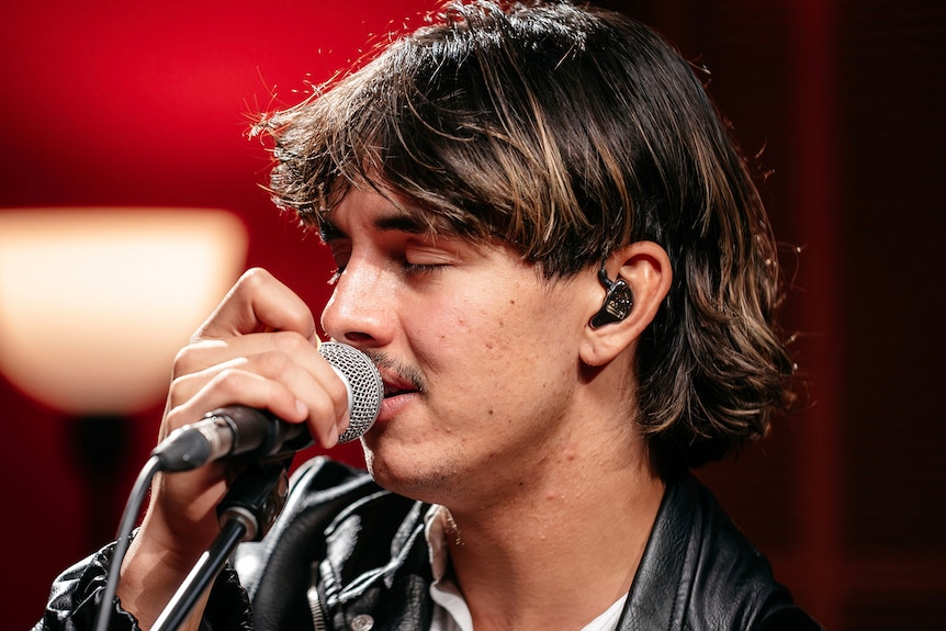 Close up of person singing into a microphone with their eyes closed in a studio