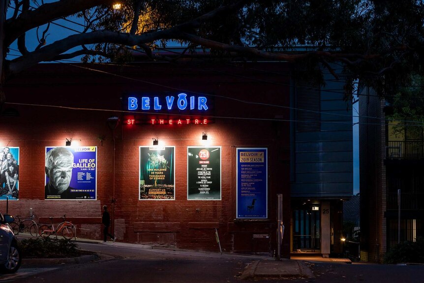 An outside shot of a theatre at night with lights and posters.