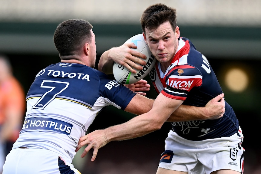 A Sydney Roosters NRL player holds the ball as a North Queensland opponent attempts to tackle him.