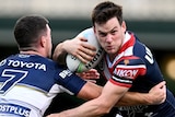 A Sydney Roosters NRL player holds the ball as a North Queensland opponent attempts to tackle him.