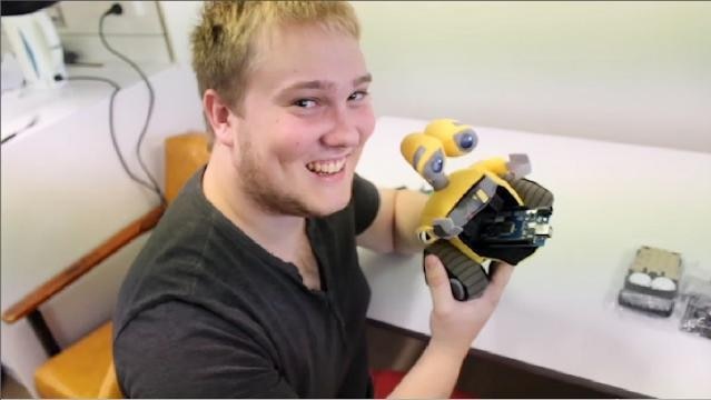 A young man holds a small robot