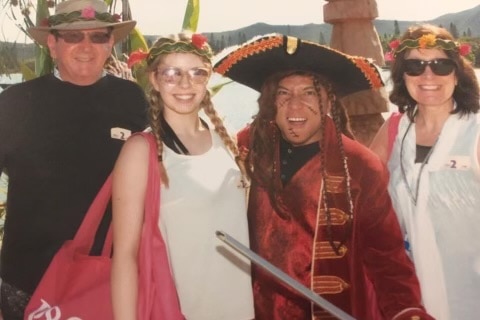 Caitlin Dennis on her first cruise with her family. They're wearing palm fronds in their hair and pose with a pirate.