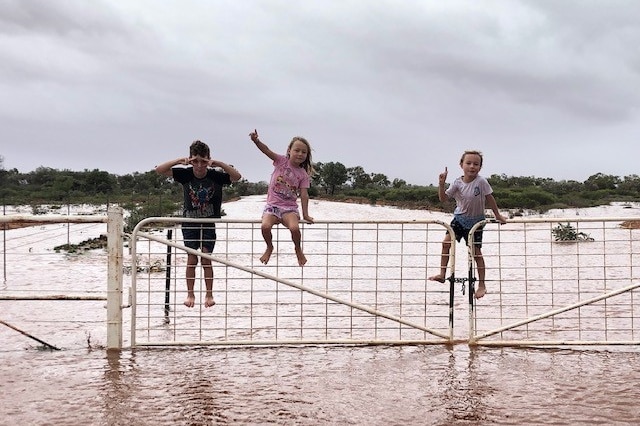 three kids on a gate surrounded by floodwaters.