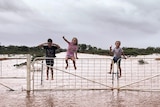 three kids on a gate surrounded by floodwaters.