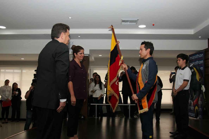 Klaus Jungbluth stands with the flag of Ecuador at a presentation ceremony.