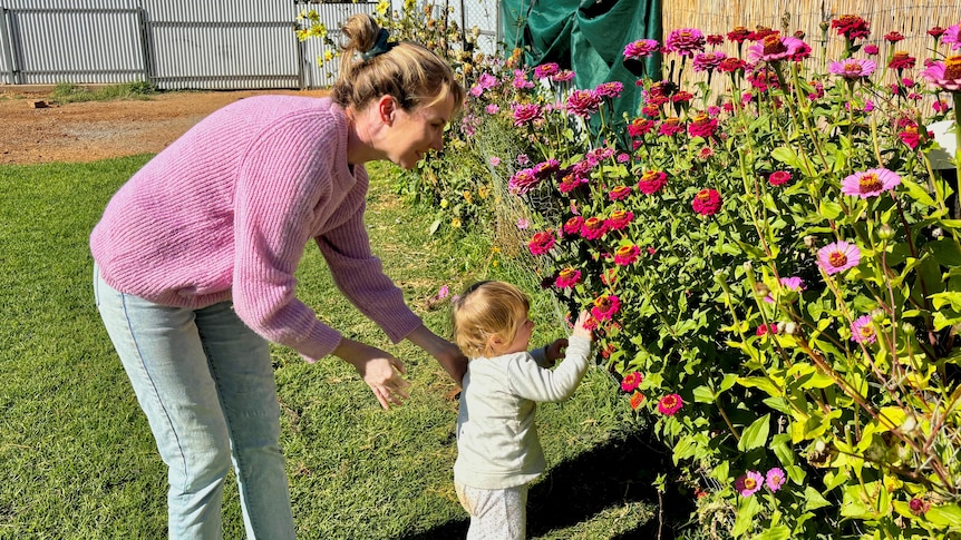 A woman in a pink jumper and a small child look at flowers.