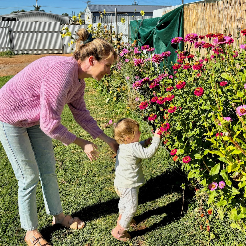 A woman in a pink jumper and a small child look at flowers.