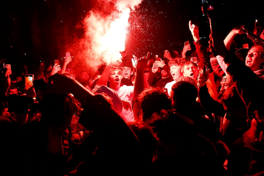 Fans light up red flares as they cheer.