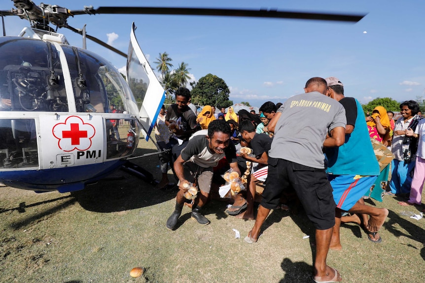 People affected by the Indonesia tsunami collect food aid delivered by helicopter.